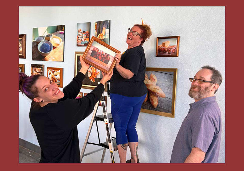 photo of three people installing an art exhibit featuring photos of bread